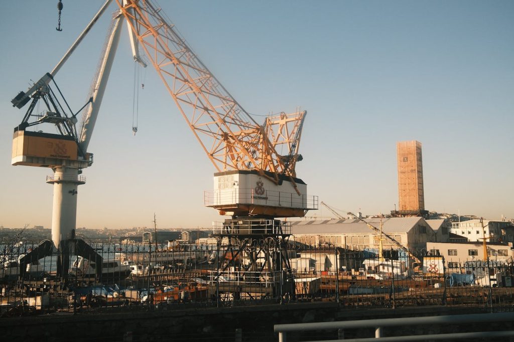 pexels-photo-29957527 Large industrial crane at a busy dockyard under a clear blue sky, showcasing modern industrial machinery.